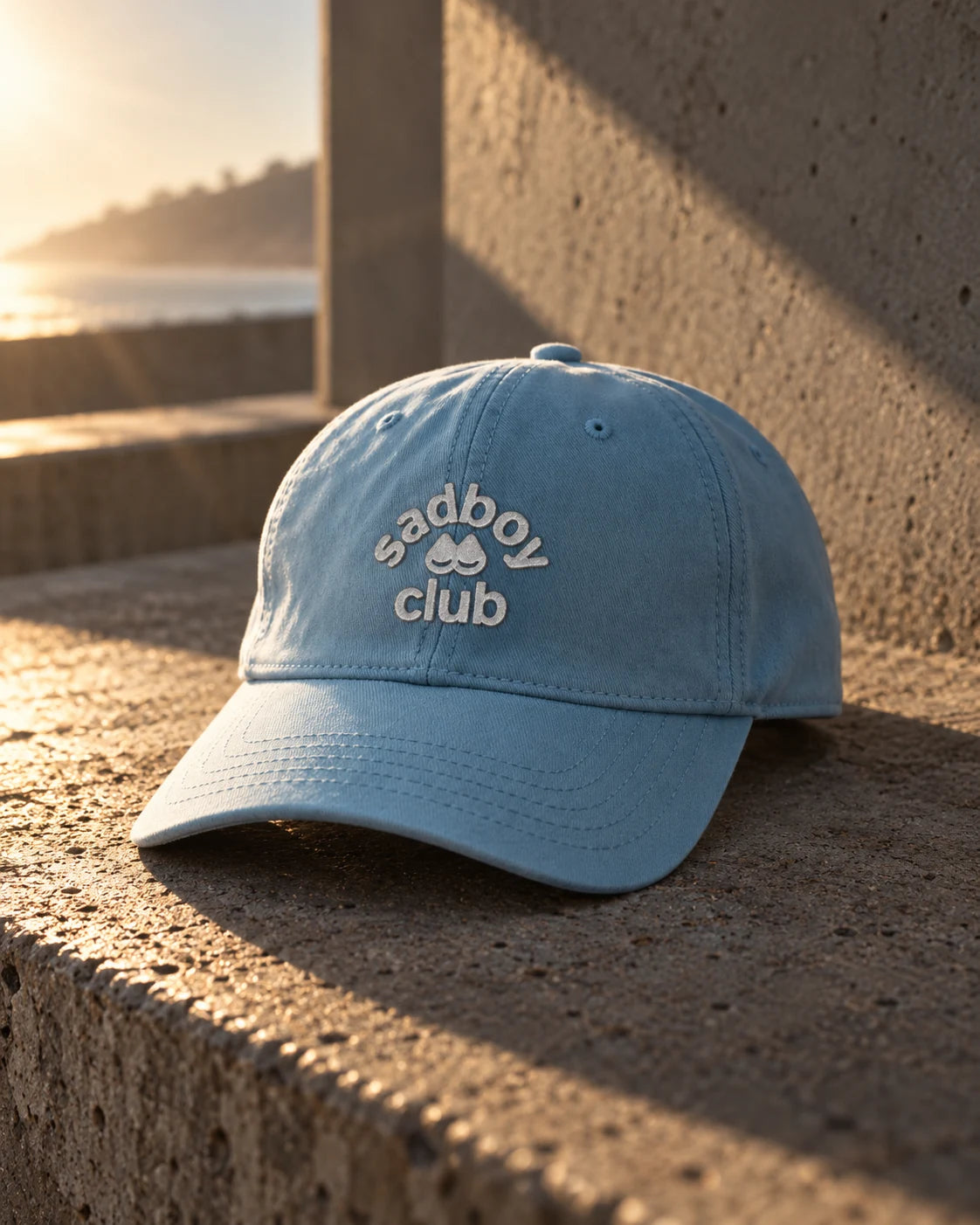 Powder-blue Sad Boy Club cap on a sunlit concrete ledge
