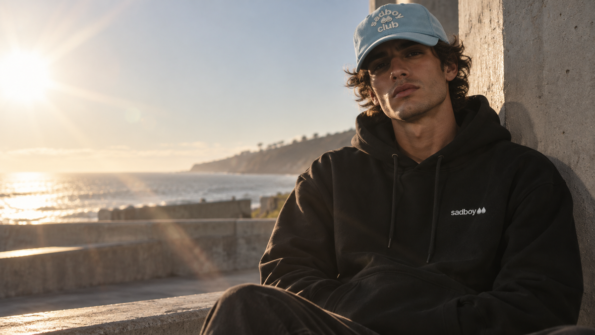 Model wearing a black Sad Boy hoodie on sunlit concrete steps